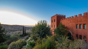 Un edificio de ladrillo rojo con una torre, rodeado de vegetación y colinas.