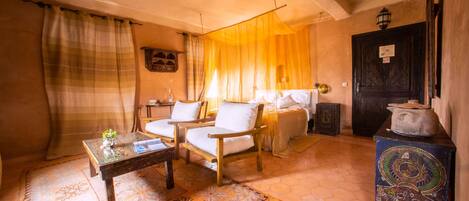 A room with a bed, two armchairs, a small table, and a decorative cabinet.