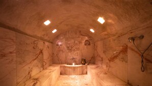 Un spa con paredes de mármol, tenuemente iluminado, que cuenta con un lavamanos central, una ducha y un pequeño rincón con un jarrón.