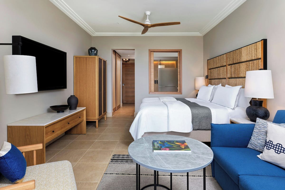 A hotel room with a bed, a sofa, a small table, a TV, a wardrobe, and a ceiling fan.