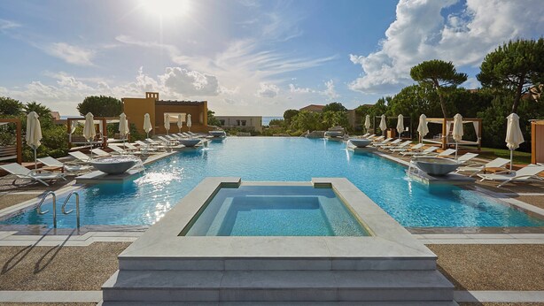 A swimming pool with lounge chairs and umbrellas, surrounded by buildings and trees. - The Westin Resort, Costa Navarino (Trifylia)
