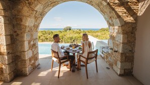 A stone archway leading to a dining area with a pool view. - The Westin Resort, Costa Navarino (Trifylia)
