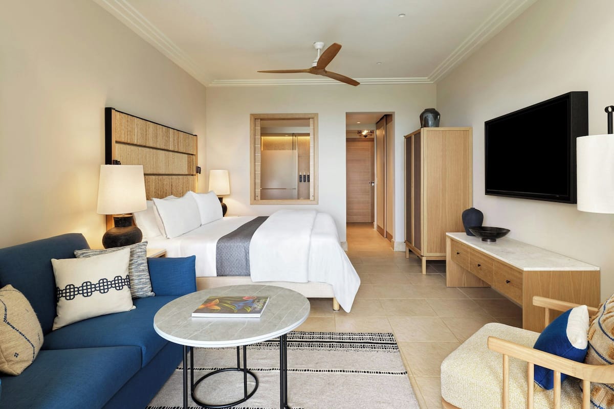 A hotel room with a bed, a sofa, a desk, a TV, and a ceiling fan.