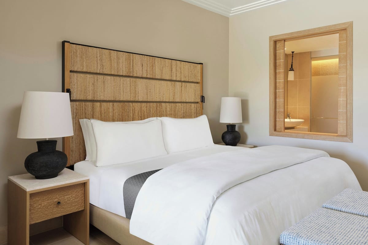 A hotel room with a large bed, two bedside tables with lamps, a wooden headboard, and a mirror on the wall.