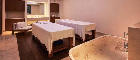 A spa room with two beds, a large bathtub, and a mirror above the beds.