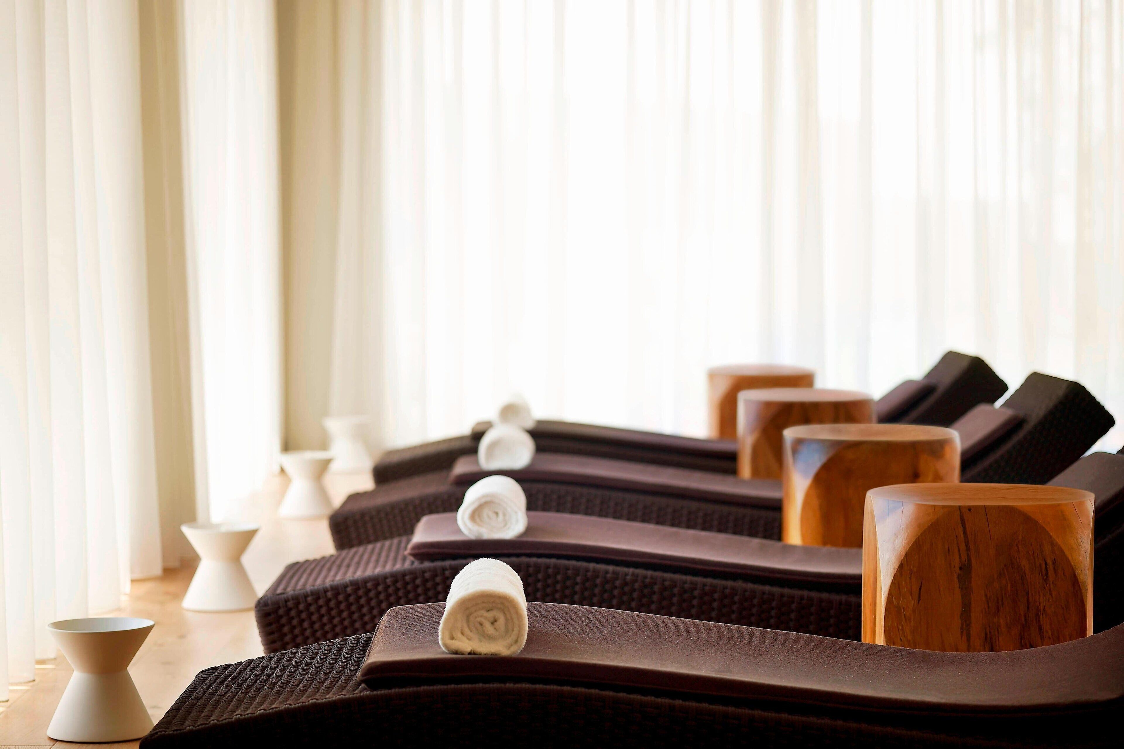 Une rangée de fauteuils de massage avec des panneaux latéraux en bois et une serviette blanche sur l’un d’eux.