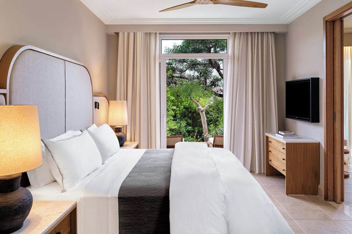 A modern hotel room with a large bed, a TV, a desk with drawers, and a window with curtains.
