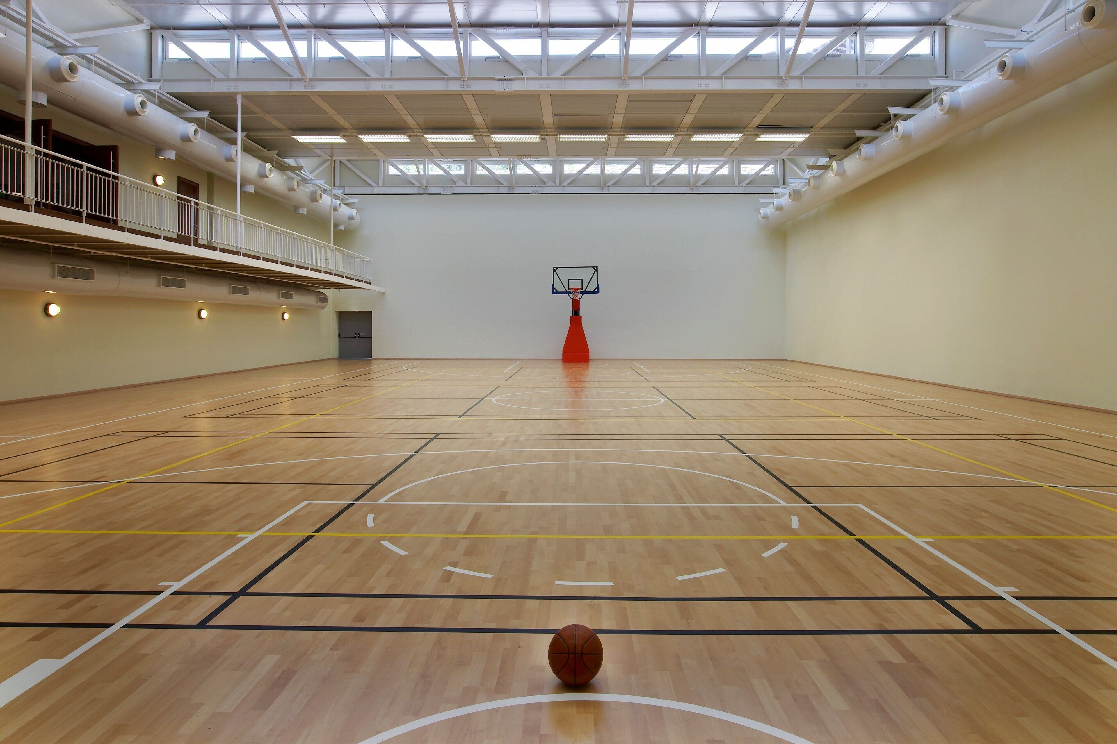 An indoor basketball court with a wooden floor, a basketball hoop, and a balcony with railings.