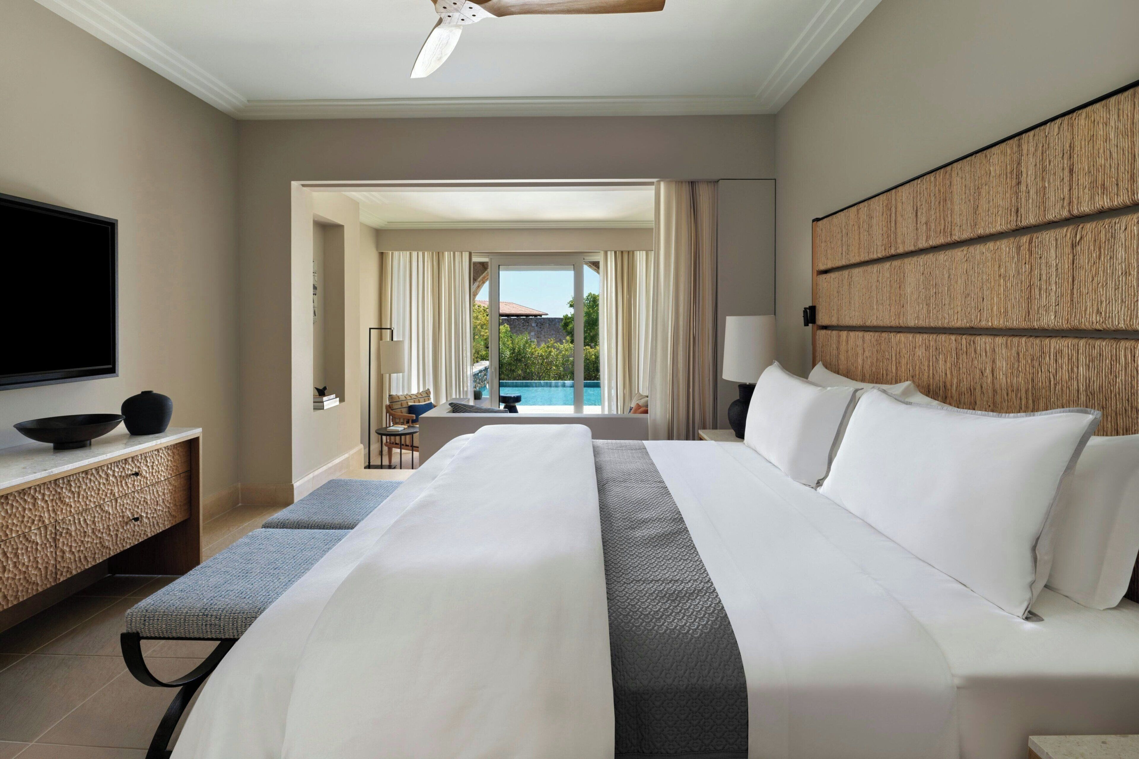 A hotel room with a large bed, a flat-screen TV, a dining table, and a view of the outdoors.