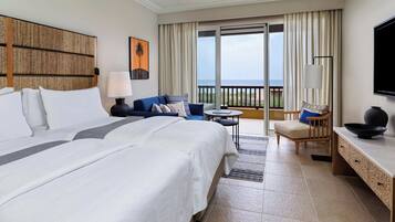 Quarto de hotel com uma cama grande, um sofá, uma mesinha, uma cadeira, televisão e varanda com vista.