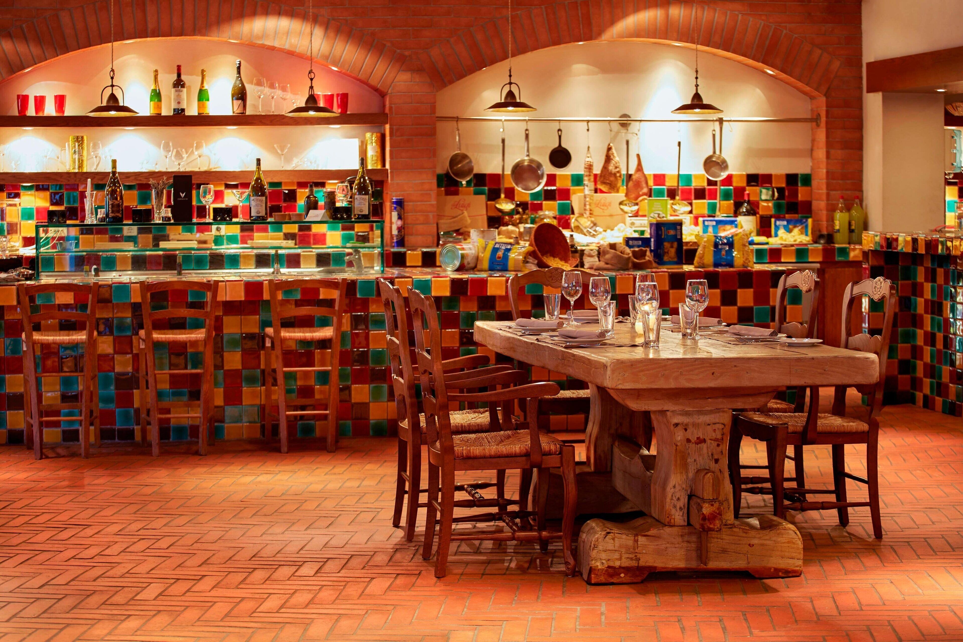 A restaurant with a colorful mosaic wall, wooden chairs, and a central table.