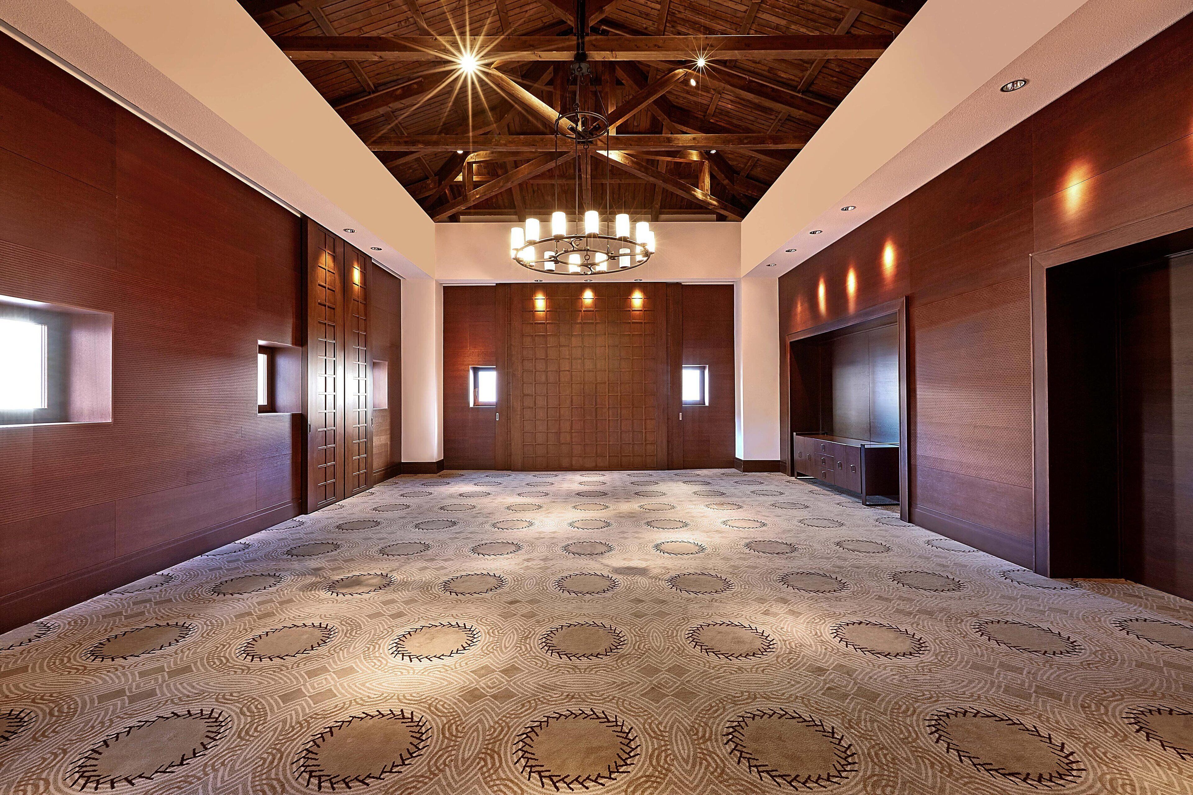 A spacious hallway with a patterned carpet, wooden walls, and a central chandelier.