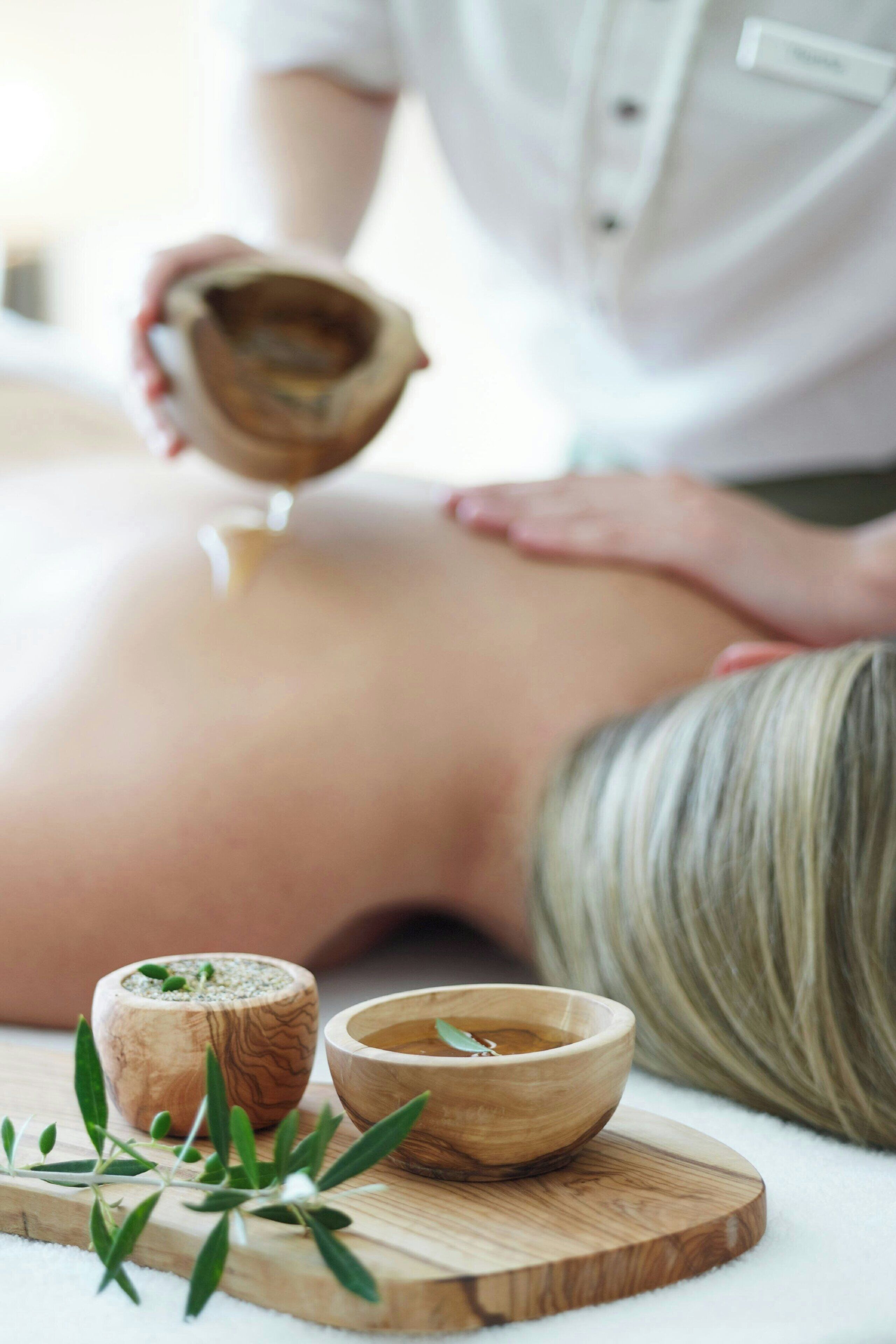 En person modtager massage med en træskål og en lille beholder på en træplade.