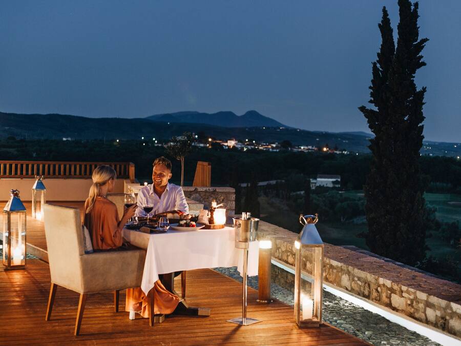 Una pareja cenando en una mesa al aire libre, con vistas a un paisaje montañoso.