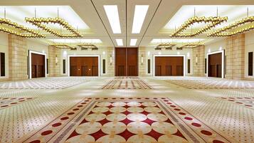 A spacious hotel lobby with a large patterned carpet, symmetrical chandeliers, and a central wooden panel.