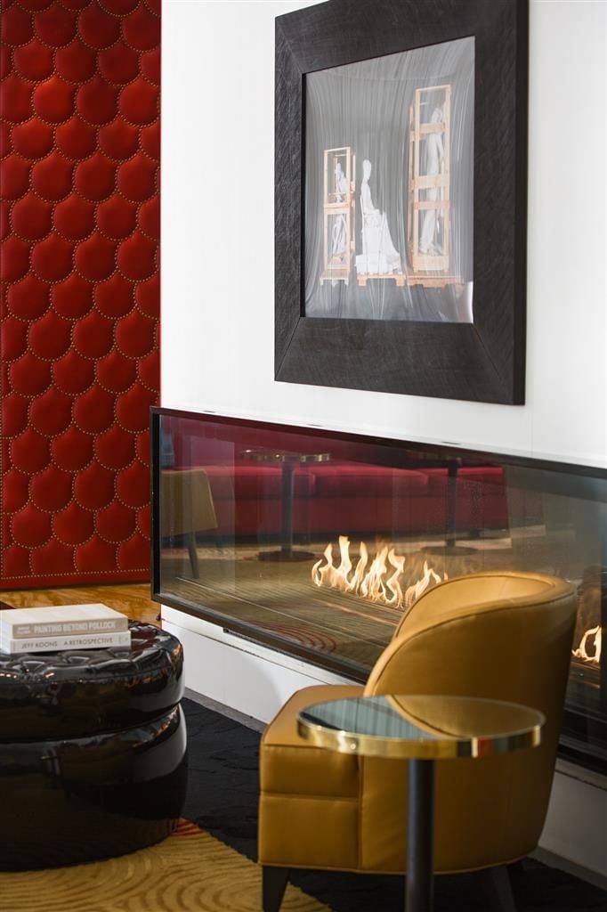 A modern living room with a fireplace, a red textured wall, and a framed artwork above it.