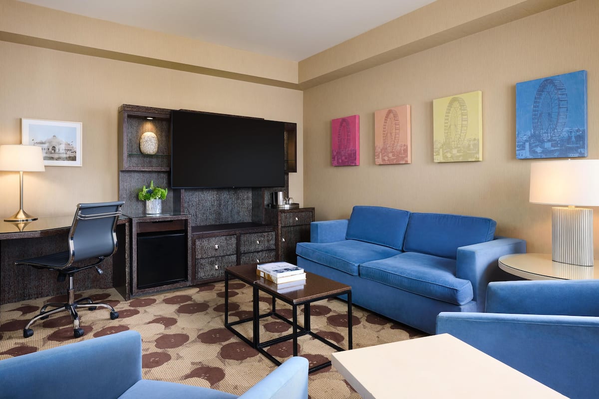 Een hotelkamer met een blauwe bank, een bureau met lamp, een flatscreen-televisie en kunstwerken aan de muren.