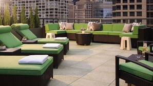 A rooftop lounge with green cushioned seating, a small round table, and a view of city buildings. - The Royal Sonesta Chicago River North (Chicago)