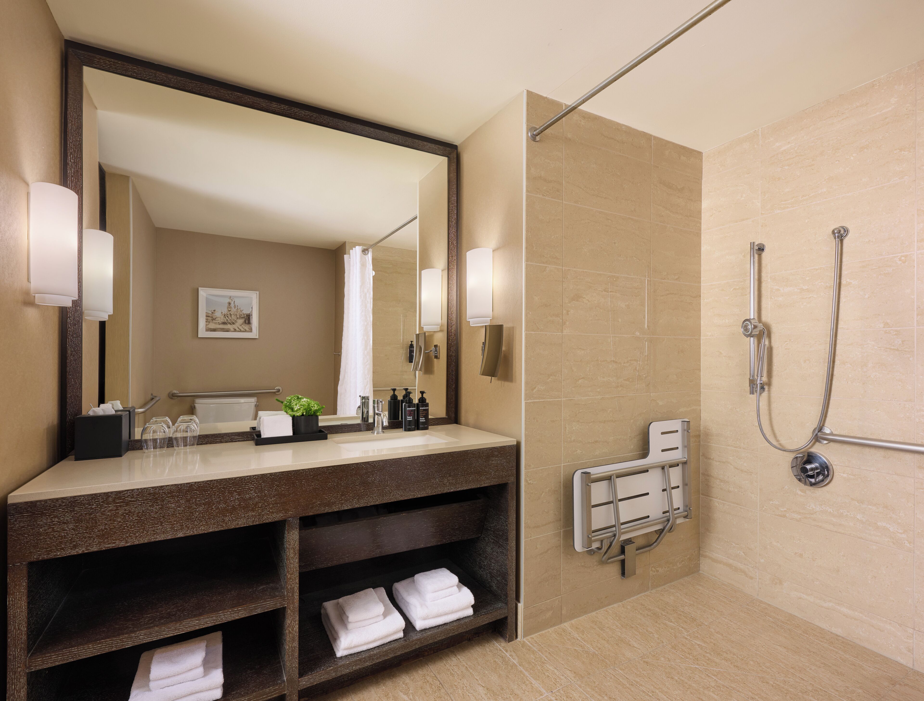 Un baño moderno con un espejo grande, un mueble de tocador con lavamanos, una ducha con cabezal de ducha manual y un perchero para toallas.