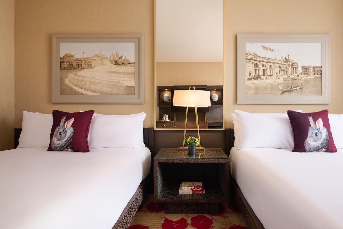 Een hotelkamer met twee bedden, elk voorzien van een kussen met een konijndesign. Er hangen ingelijste foto’s aan de muren, een nachtkastje met een lamp, en een klein boekje getiteld 'KINFOLK JOURNEYS'.