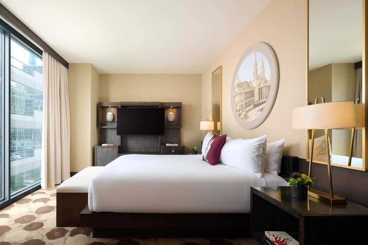 Een hotelkamer met een groot bed, een televisie, een bureau en uitzicht op de stad.