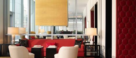 A modern hotel lobby with a red sofa, white armchairs, and a large yellow pendant light.