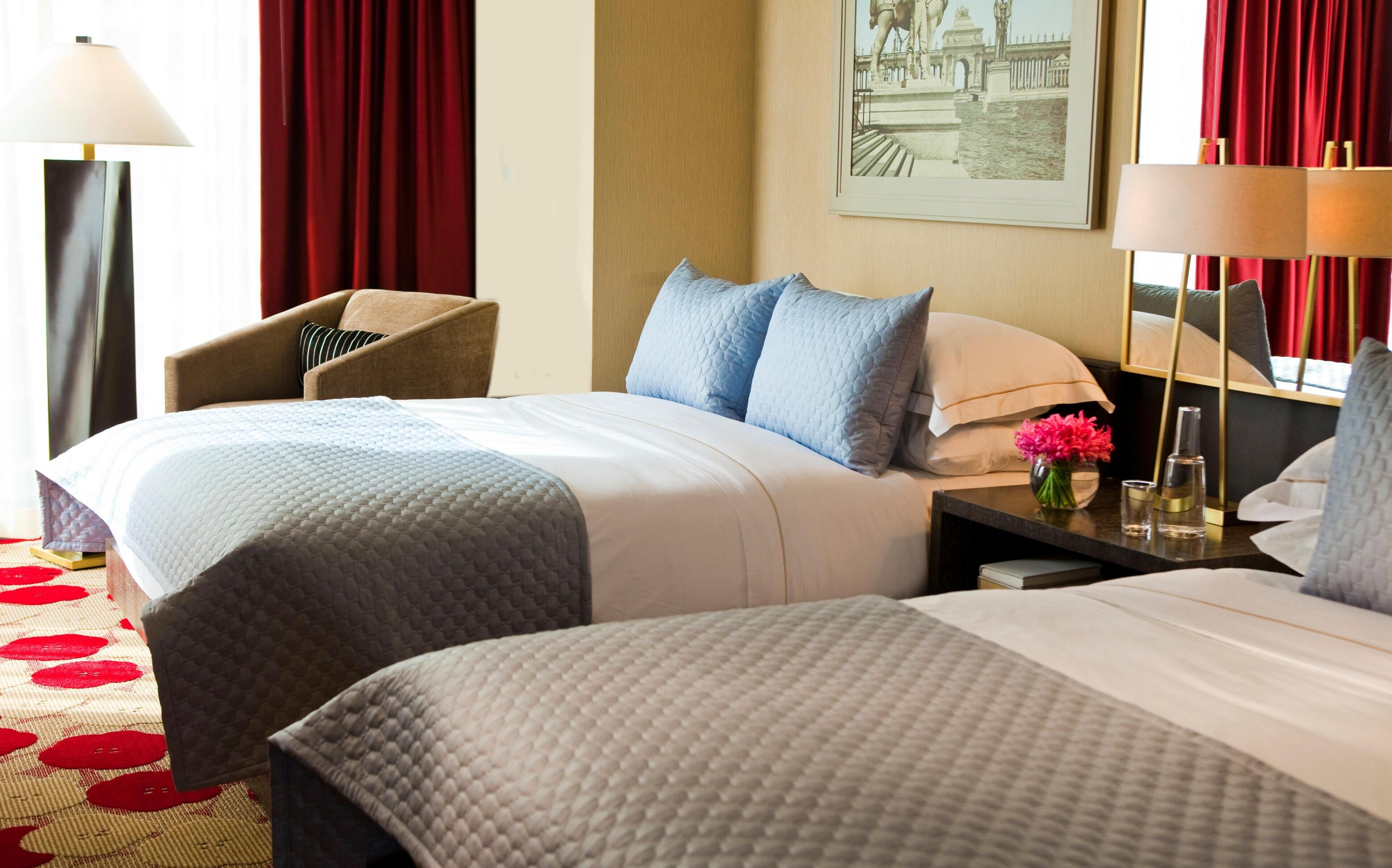 Een hotelkamer met twee bedden, een stoel, een nachtkastje met een bloemenvaas en een schilderij aan de muur.