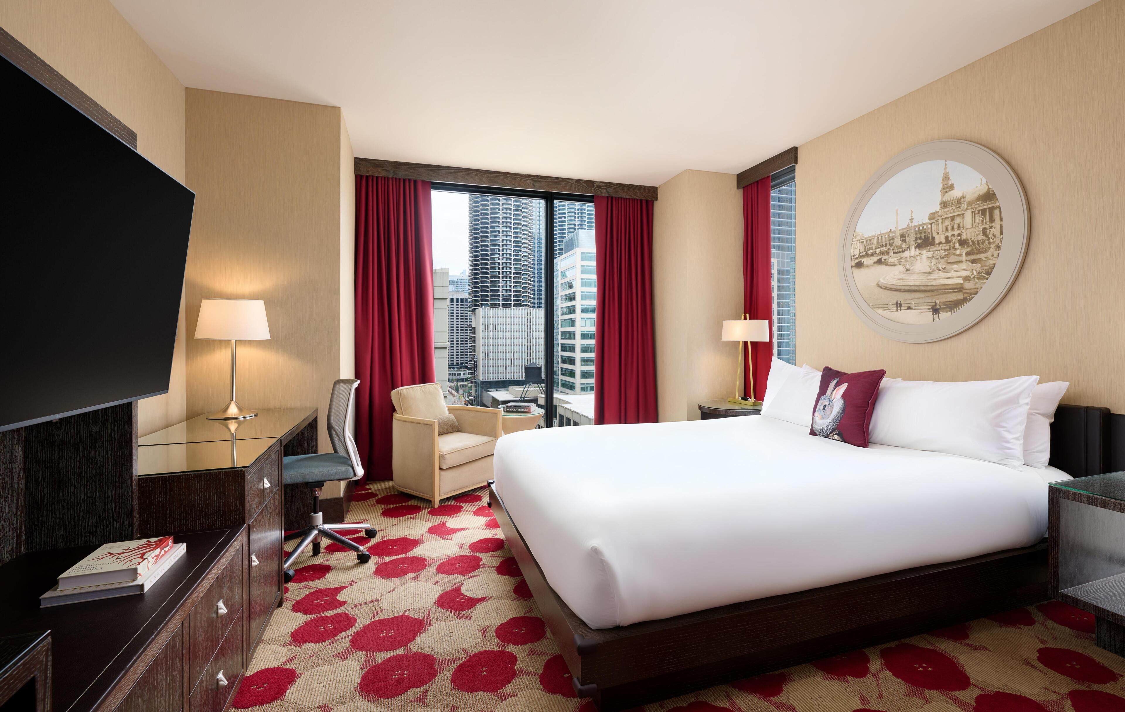 Een hotelkamer met een groot bed, een bureau, een stoel, een televisie en een raam met uitzicht op de stad.