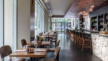 A modern restaurant with long tables, bar area, and large windows.