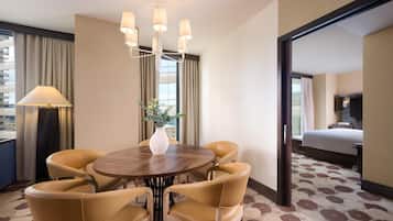 A hotel room with a round dining table, six chairs, a vase with greenery, a lamp, and a bed.