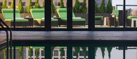A poolside area with lounge chairs and a reflection of the surrounding buildings.