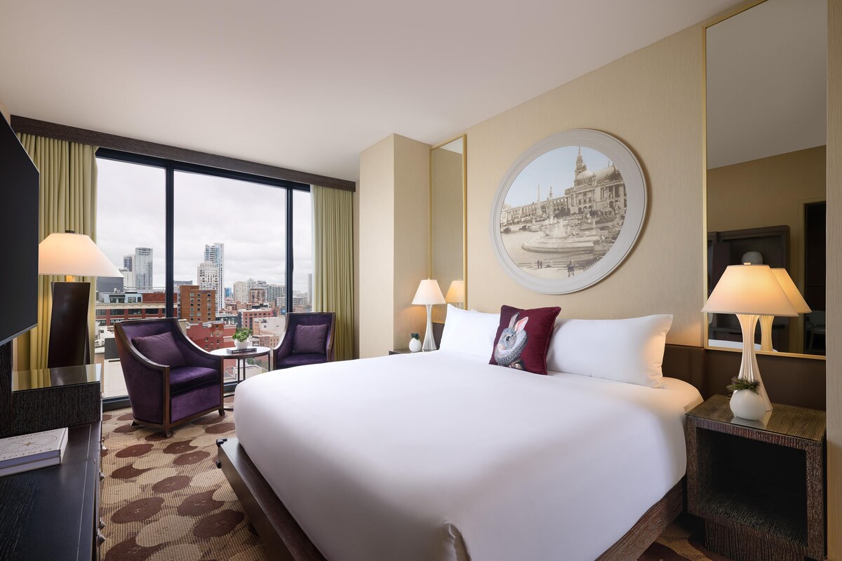 Hotelkamer met een groot bed, twee stoelen, een bureau, een televisie en uitzicht over de stad.