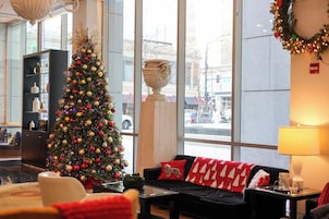 A hotel lobby with a large Christmas tree, a sofa with red and white pillows, a glass coffee table, and a large window with a view of the street.