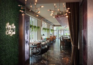 Een modern restaurantinterieur met een groene wand, hangende lampen en een lange eethoek.