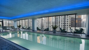 A modern indoor pool area with clear glass walls, lounge chairs, and a view of city buildings. - The Royal Sonesta Chicago River North (Chicago)