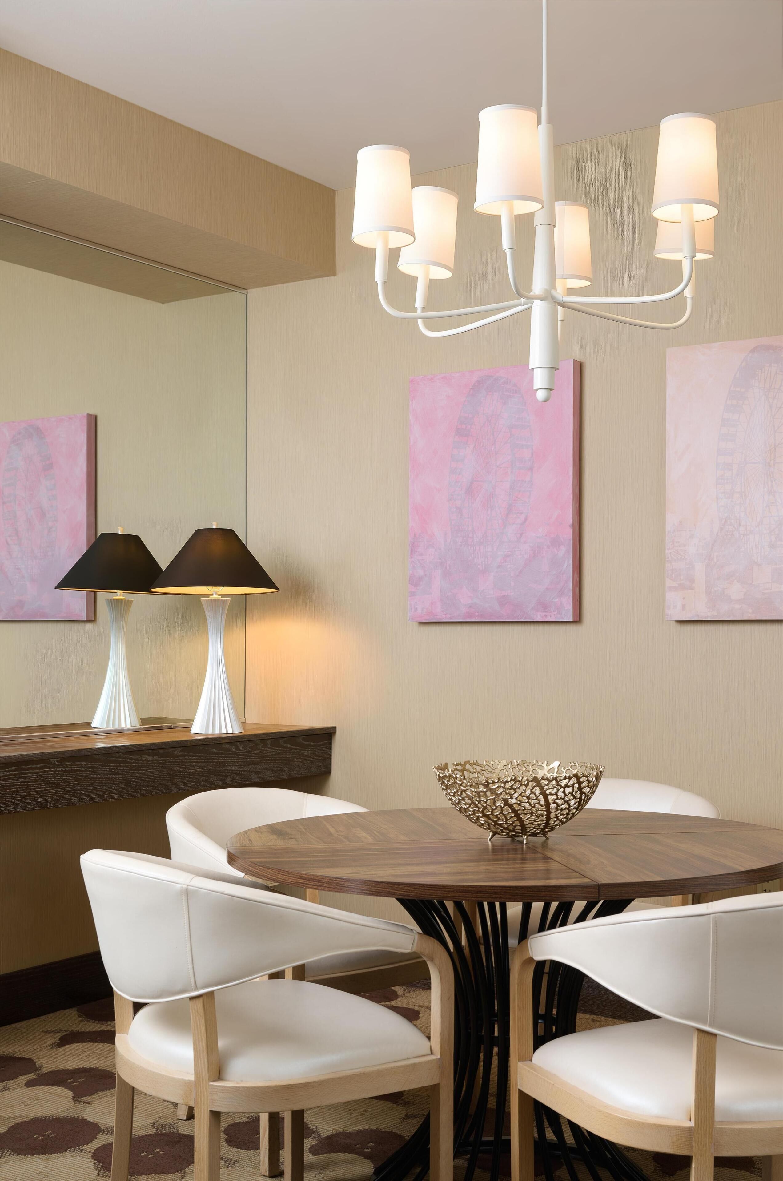 Un comedor con una mesa redonda, sillas blancas, una araña y pinturas abstractas en la pared.