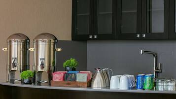 Zona de bar con dos máquinas de espresso, una pequeña planta en maceta y diversas bebidas y aperitivos.