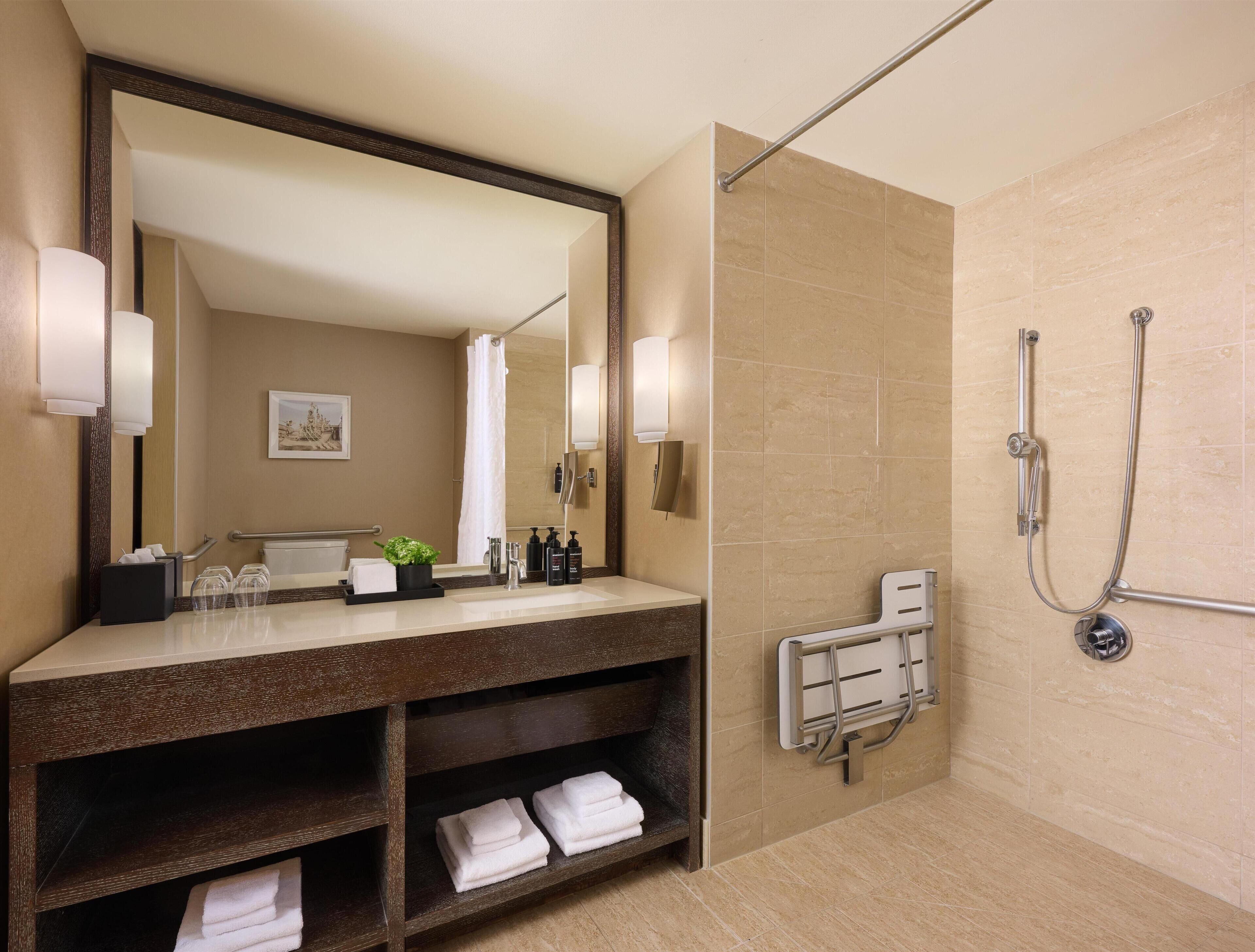 Un baño moderno con un espejo grande, una ducha con cabezal de ducha de mano y un perchero para toallas.
