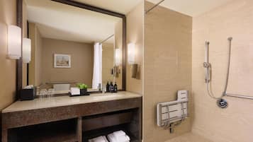 Un baño moderno con un espejo grande, una ducha con cabezal de ducha de mano y un perchero para toallas.