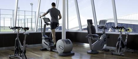 A gym with cardio machines, large windows, and a wooden floor.