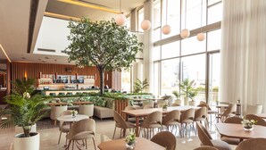 Un moderno vestíbulo de hotel con una gran palmera en su interior, asientos cómodos y una zona de bar.