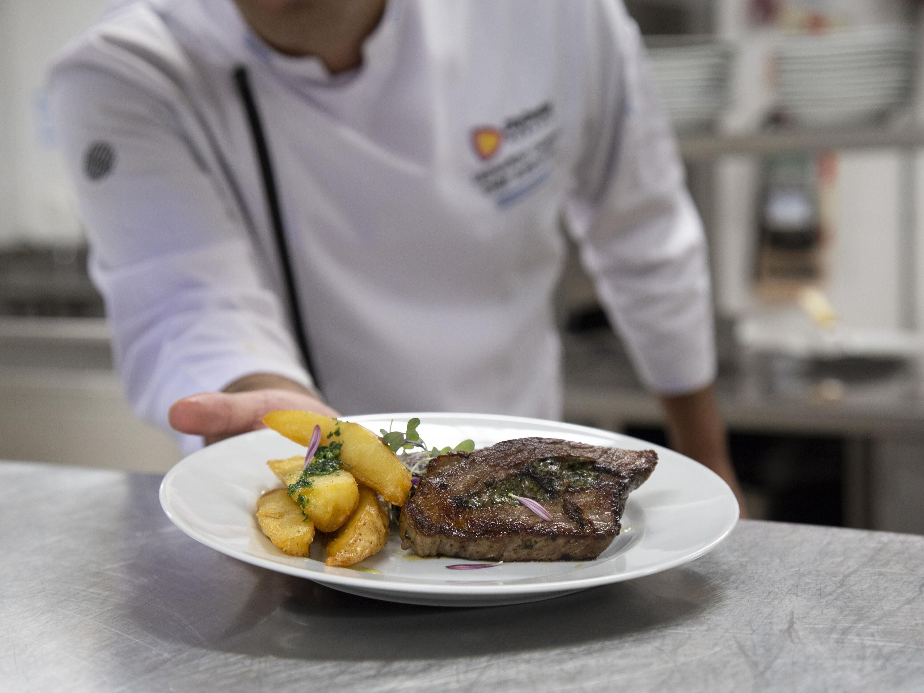 Un chef présente un plat composé de steak et de pommes de terre.