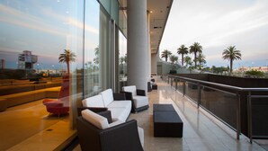 Un área de descanso moderna al aire libre con asientos y vista a palmeras y un horizonte urbano distante.
