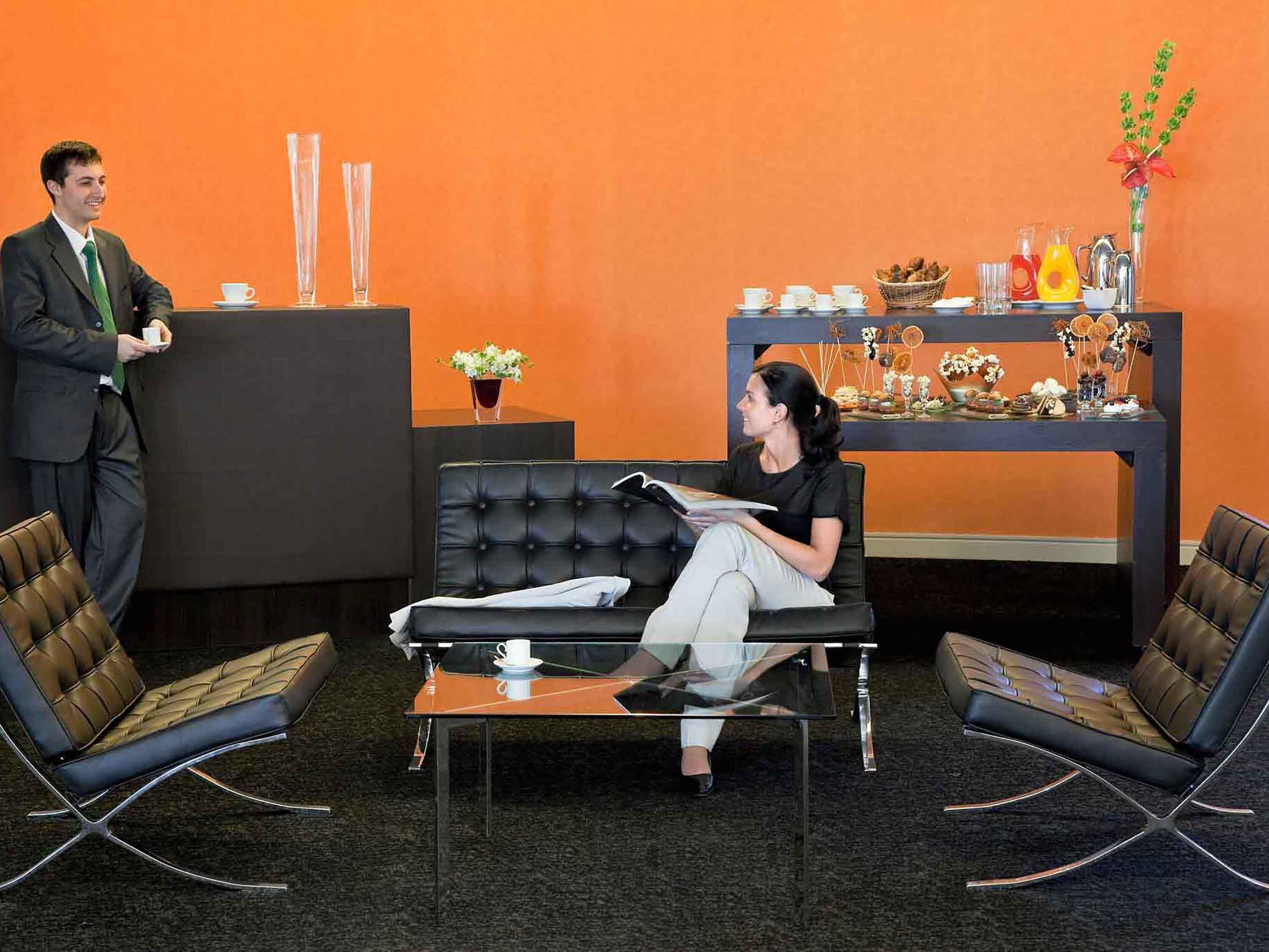 A reception area with a black leather sofa, two chairs, a reception desk, and a decorative shelf with various items.