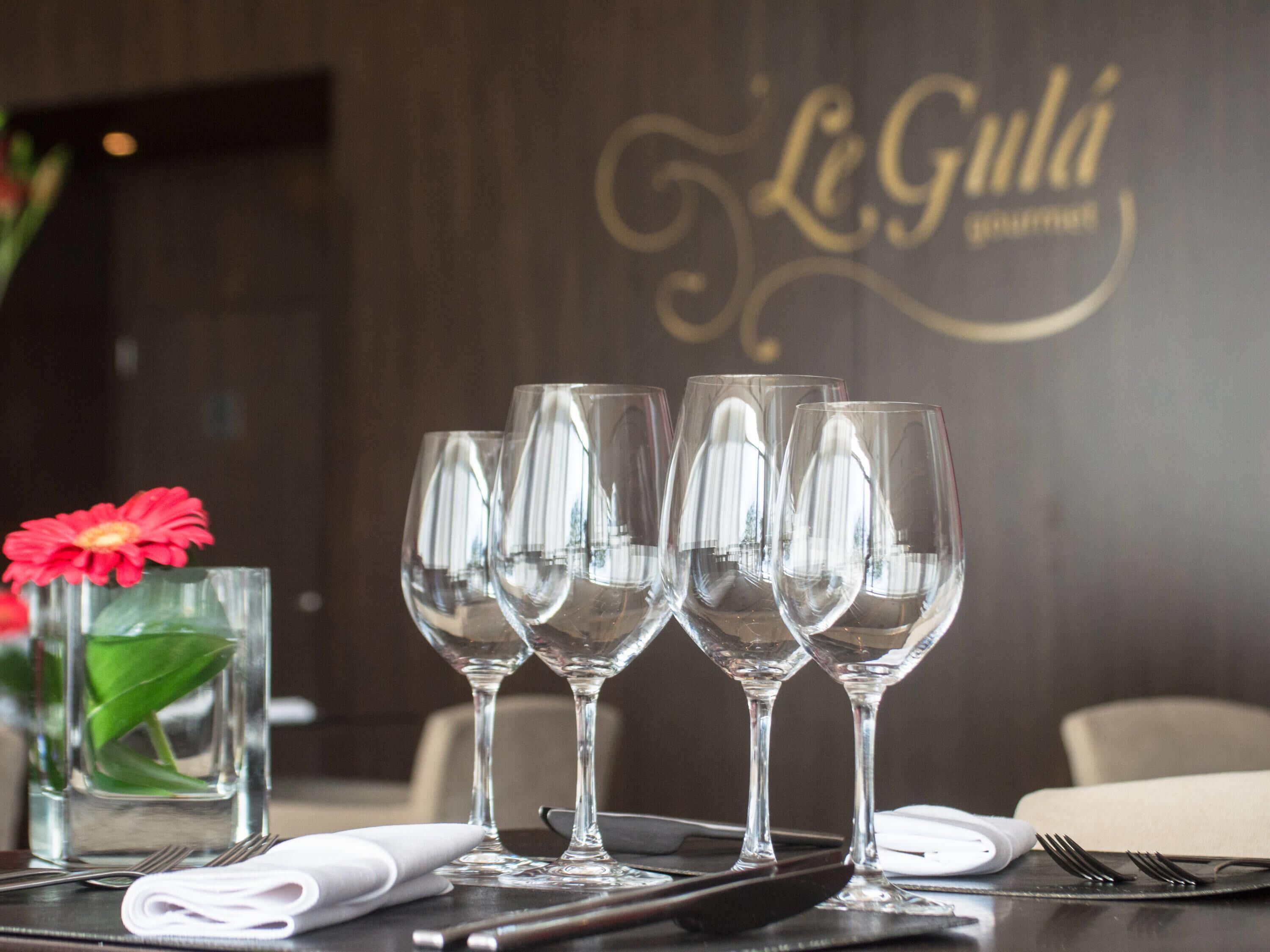 Una mesa dispuesta con copas de vino, un florero con una flor roja y una servilleta.