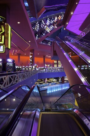 Un atrio interior con varios niveles conectados por escaleras mecánicas, con una fuente central y diversas máquinas de videojuegos.