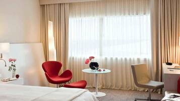 Habitación de hotel con cama, escritorio, dos sillas, una mesita y ventana con cortinas.