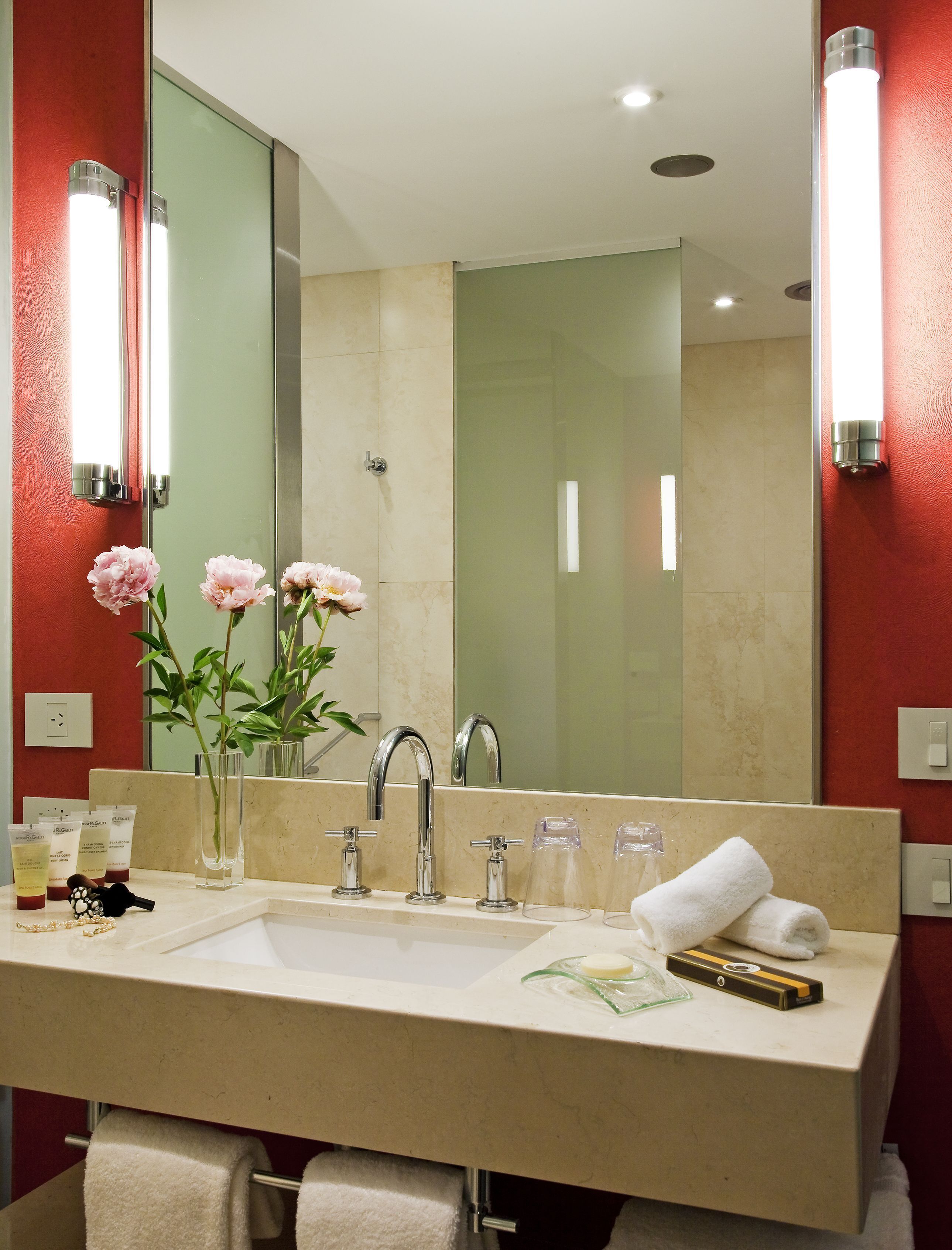 Un baño con un espejo grande, un lavabo, un perchero para toallas y un florero con flores.