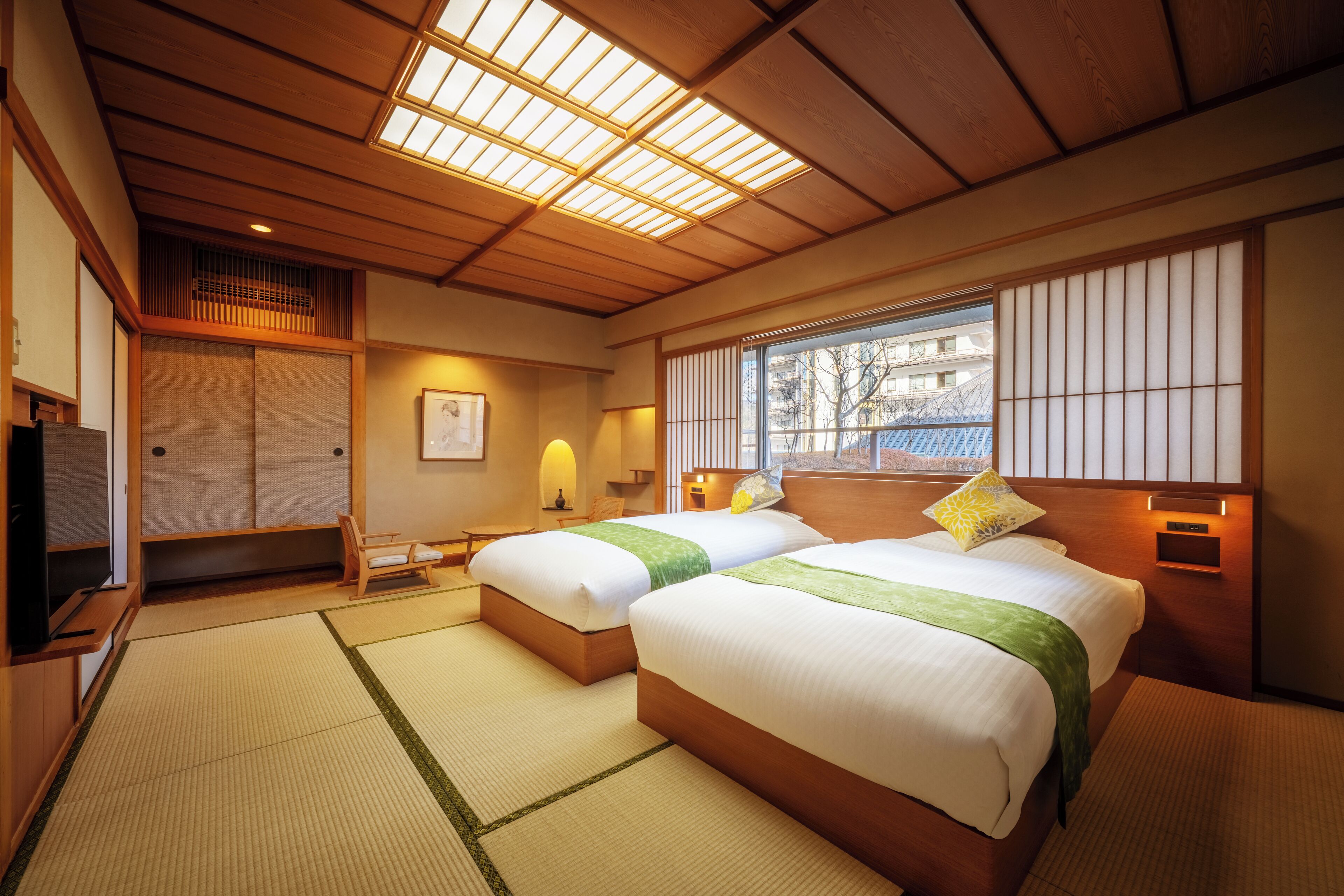 A hotel room with two beds, tatami mats, a television, and a window with a view of buildings.