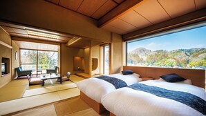 Hotelkamer met twee bedden, een zithoek met tatami-matten en een groot raam met uitzicht op een bergachtig landschap.